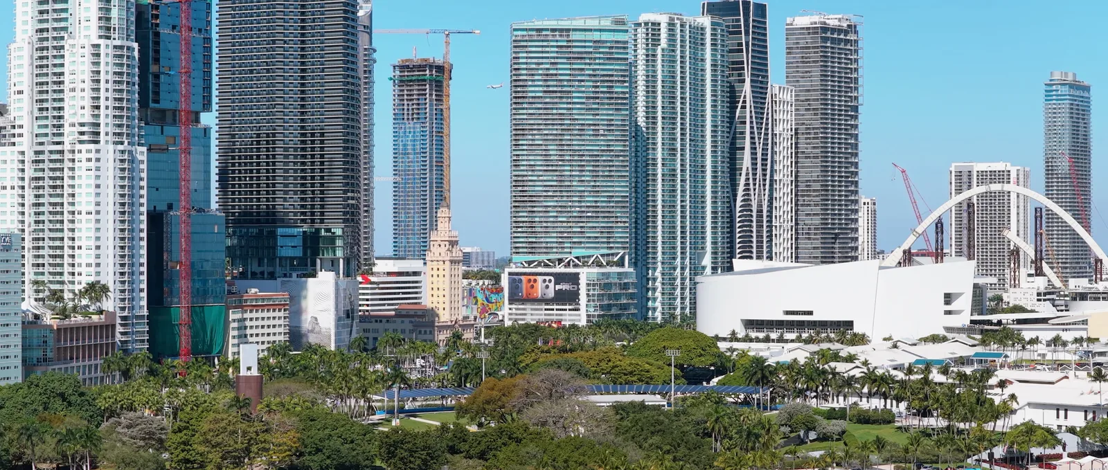 Downtown Miami towers rising behind Bayfront Park, palms and lawns in front, the bay at the bottom of the frame.